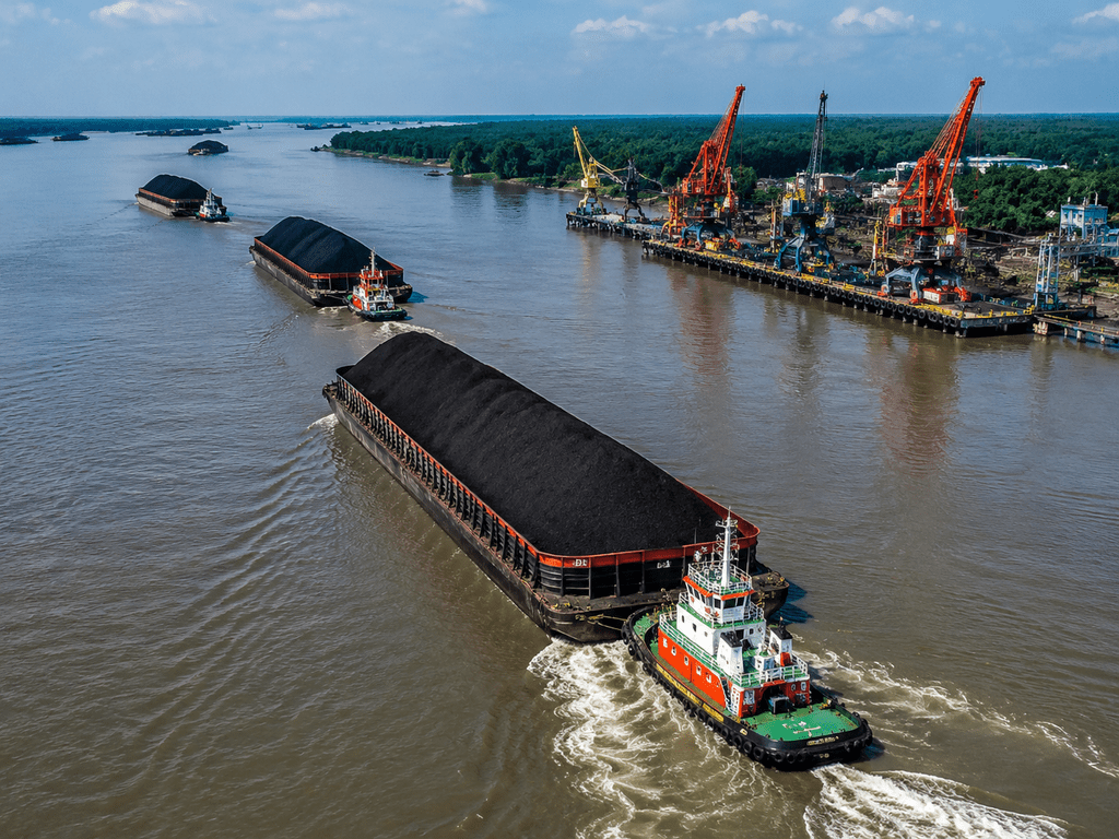 Iring-iringan kapal tongkang batu bara di jalur logistik sungai menuju pelabuhan transshipment ekspor.